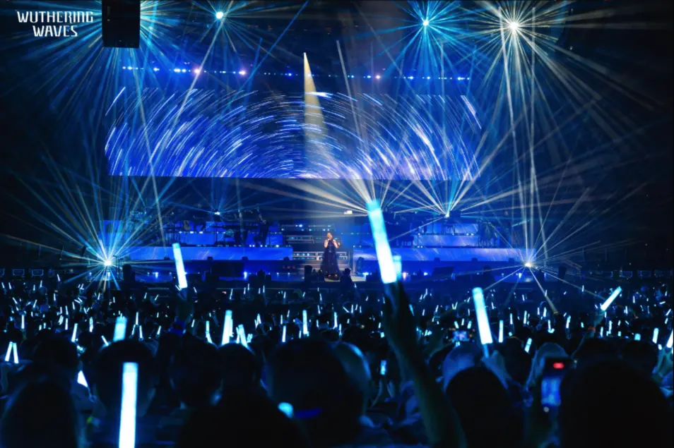 Concert audience holding blue lightsticks under blue stage lights