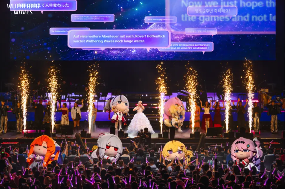 Concert audience holding pink lightsticks, with performers and character mascots on stage